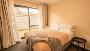 A hotel room with a bed, a small side table, and a view through a window with curtains.