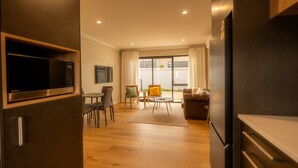 A modern kitchen with built-in appliances, a dining area with a table and chairs, and a living room with a sofa and a window.