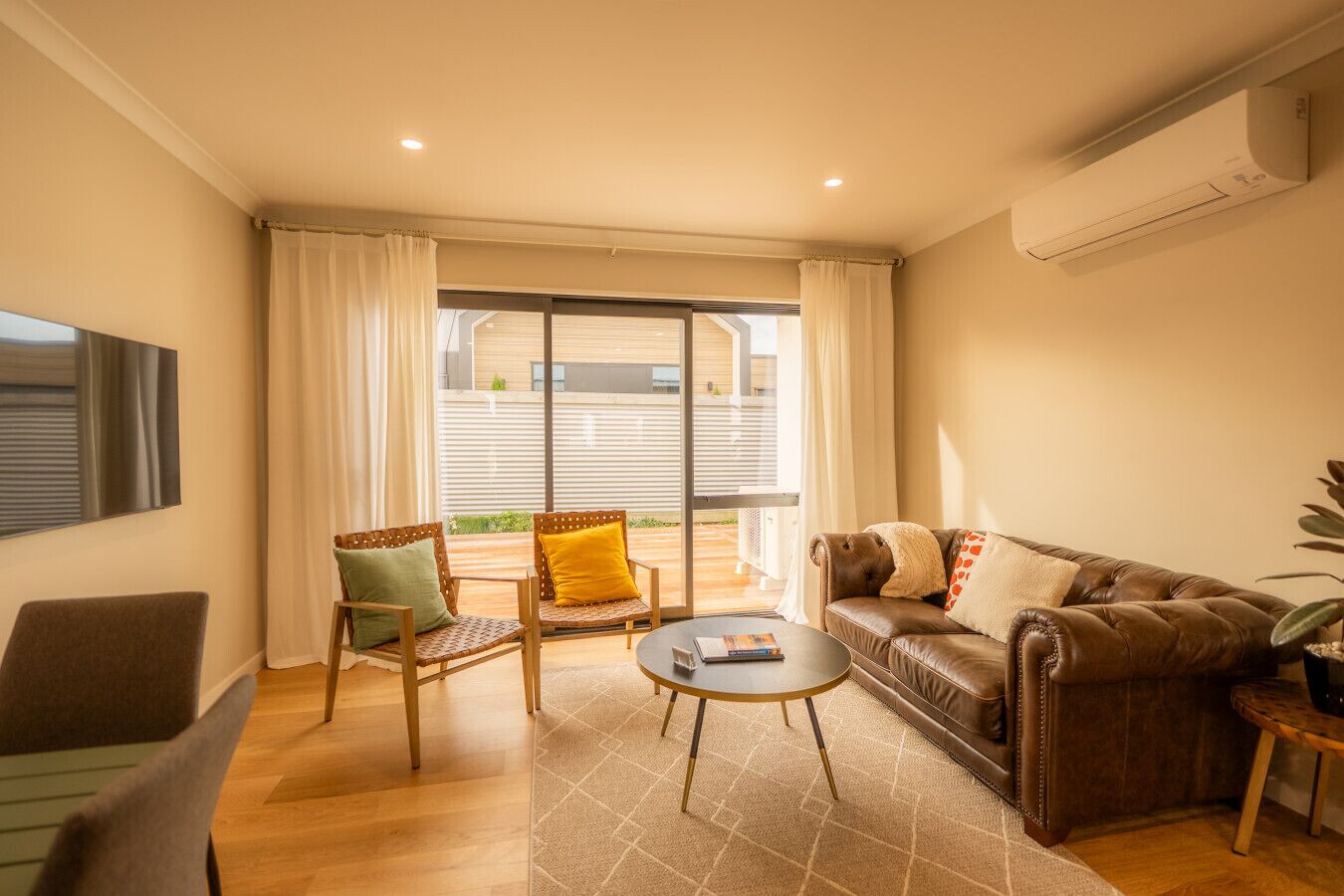 A modern living room with a leather sofa, two armchairs, a coffee table, and a large window with curtains.