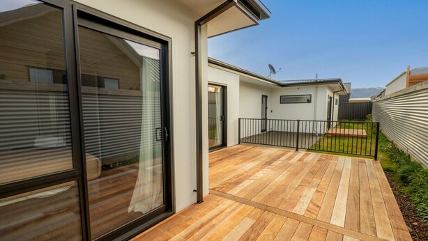 A modern residential building with a wooden deck, sliding glass doors, and a metal fence.