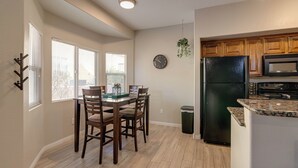 Une cuisine moderne avec un réfrigérateur noir, des meubles de rangement en bois et un coin repas comprenant une table et des chaises.