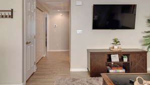 Un couloir doté d’un plancher en bois, d’un téléviseur fixé au mur et d’un meuble en bois foncé sur lequel est posée une plante.
