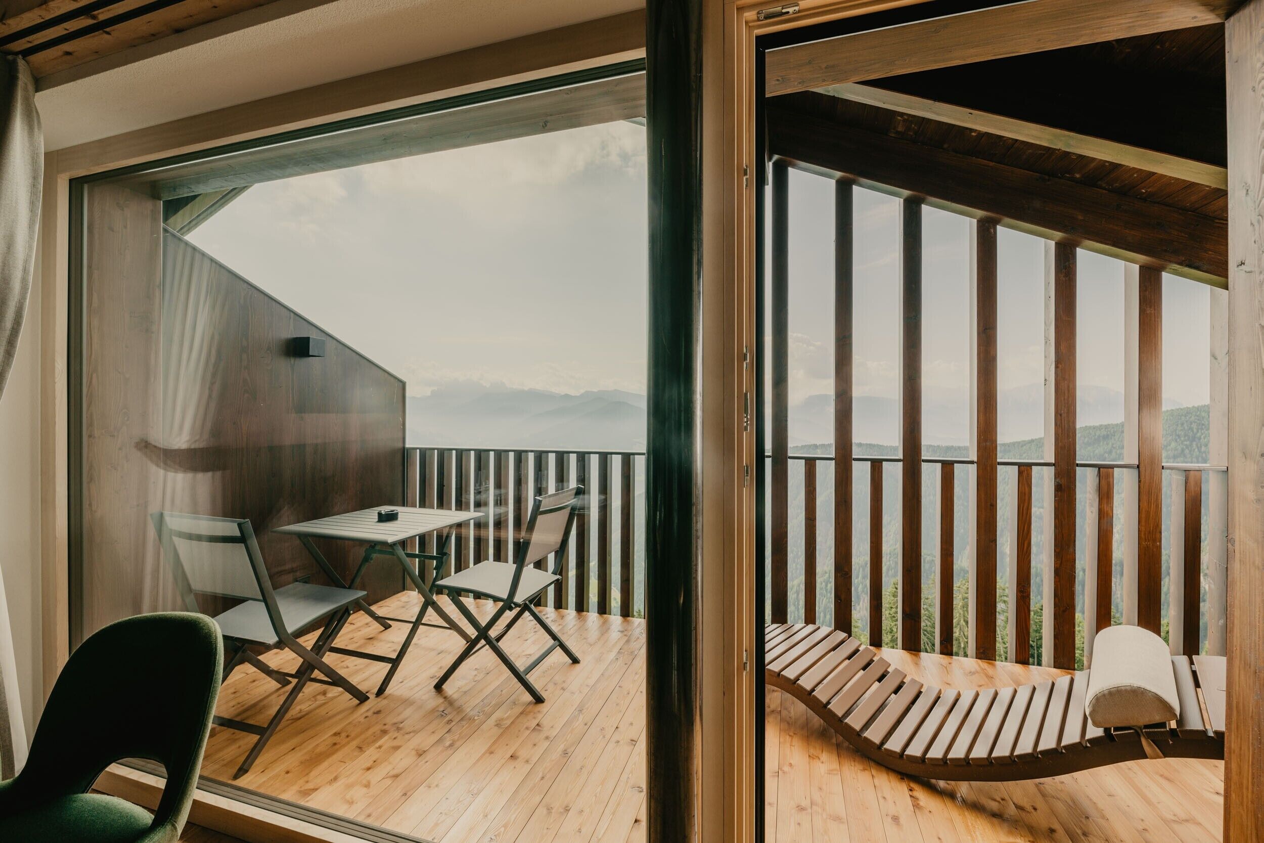Un balcon doté d’un plancher en bois, d’une table avec des chaises et d’un coin salon avec des coussins.