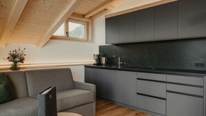 Een moderne keuken met grijze kastjes, een houten plafond en een bank met een afstandsbediening op een tafel.