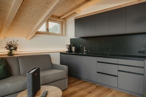 A modern kitchen with grey cabinets, a wooden ceiling, and a sofa with a remote control on a table.