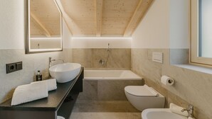 Een moderne badkamer met een houten plafond, een grote spiegel, een vrijstaand bad, een toilet en een wastafel met een handdoek.