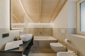 A modern bathroom with a wooden ceiling, a large mirror, a freestanding bathtub, a toilet, and a sink with a towel.
