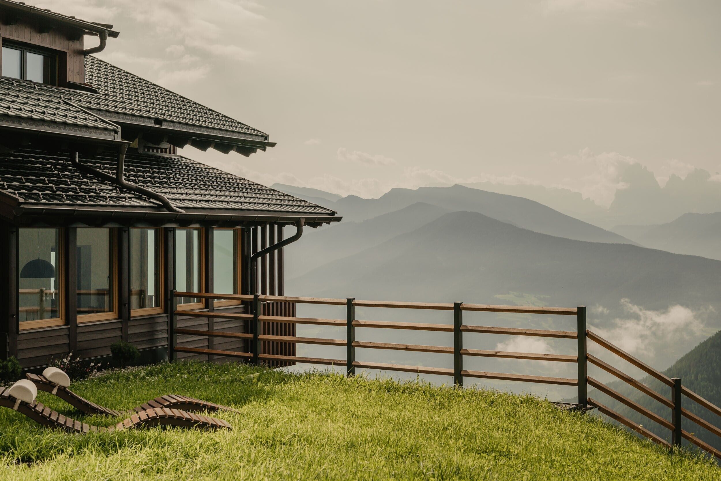 A wooden building with large windows, a wooden fence, and a grassy area.
