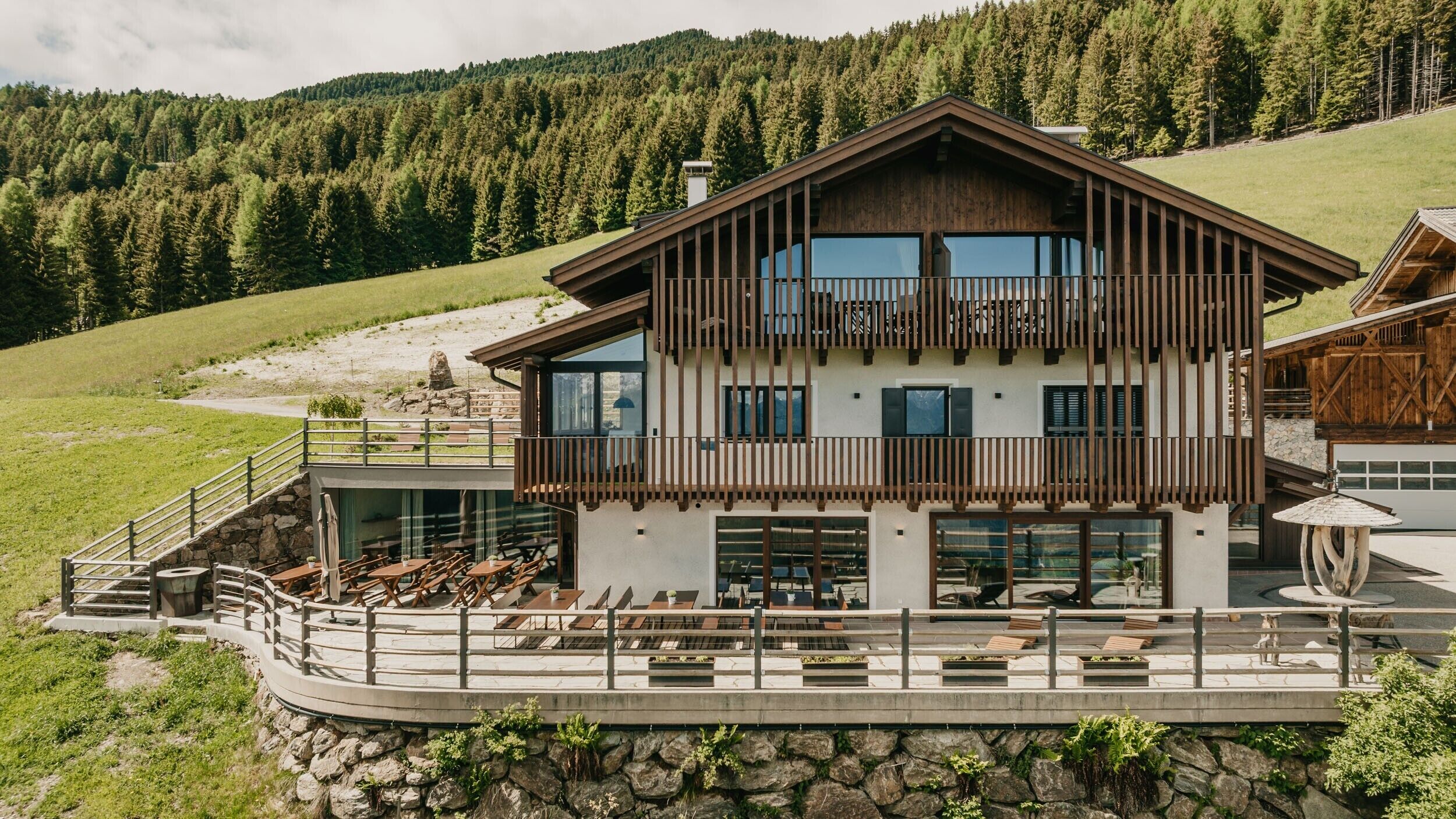 A two-story chalet with a balcony, outdoor seating, and a stone retaining wall.