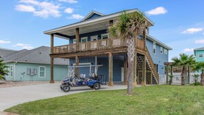 A two-story house with a balcony, a covered porch, and a golf cart parked in front. - 4/4. Pool & Golf Cart.  1st Floor Master Suite.  2 Masters Up, Boat Parking.  
 (Port Aransas)