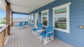 A covered porch with blue walls, white railings, and three blue cushioned chairs. - 4/4. Pool & Golf Cart.  1st Floor Master Suite.  2 Masters Up, Boat Parking.  
 (Port Aransas)
