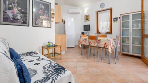 Een ruimtelijk ingerichte leefruimte met een bank, een eettafel met stoelen, een keukenhoek met een koelkast, en een kast met glazen deuren.
