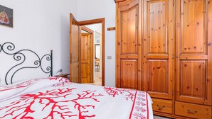 Een slaapkamer met een bed, een houten kledingkast en een deur naar een andere kamer.
