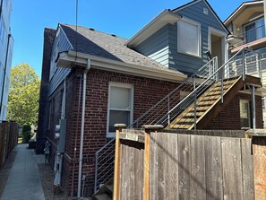 Un immeuble résidentiel avec une façade en briques, une clôture en bois et un escalier en métal menant à un balcon.