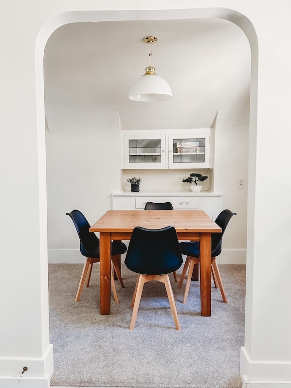 A dining area with a wooden table and black chairs, white cabinets, and a hanging light fixture.