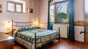 Quarto com cama, janela com cortinas, radiador e teto de madeira.