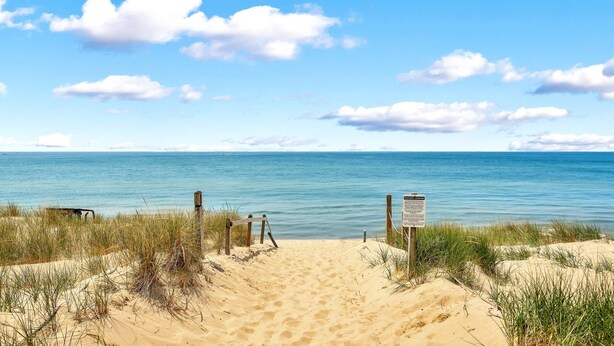 Een zandstrand met een houten hek en een bord, dat naar de oceaan wijst.