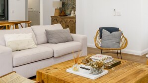 Una sala de estar con una mesa de centro de madera, un sofá blanco, una silla de mimbre y un aparador con adornos.