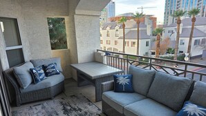 A balcony with wicker furniture, a patterned rug, and a view of palm trees and buildings.