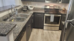 A modern kitchen with granite countertops, stainless steel appliances, and dark cabinetry.