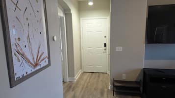 A hallway with a framed artwork, a white door, a staircase, and a TV on the wall.