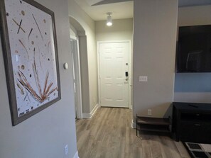 A hallway with a framed artwork, a white door, a staircase, and a TV on the wall. - Downtown Cactus Diamond (Phoenix)