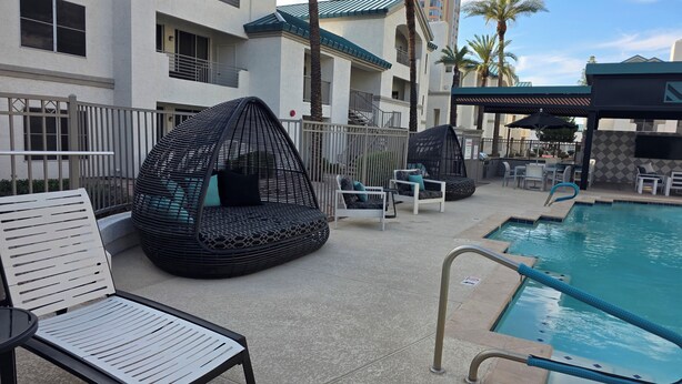 A poolside area with lounge chairs, a hanging chair, and a pool with a safety sign.