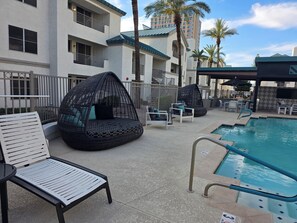 A poolside area with lounge chairs, a hanging chair, and a pool with a safety sign.