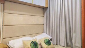 A hotel room with a bed, a headboard, an air conditioning unit, and a window with curtains. - Cozy Retreat 1-bedroom unit with pool and balcony in Mall of Asia (MOA) (Pasay)