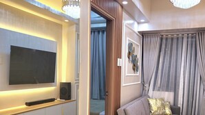 A modern living room with a flat-screen TV, a sofa, and a chandelier. - Cozy Retreat 1-bedroom unit with pool and balcony in Mall of Asia (MOA) (Pasay)
