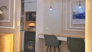 A compact kitchen with a microwave, refrigerator, and a small dining area with two chairs and a wooden table. - Cozy Retreat 1-bedroom unit with pool and balcony in Mall of Asia (MOA) (Pasay)