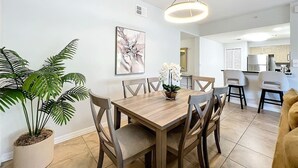 A dining area with a wooden table, chairs, a potted plant, and a hanging light fixture.