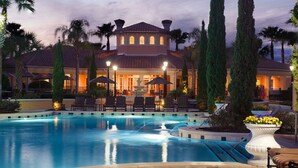 A pool area with lounge chairs, a fountain, and a building with multiple windows and a tiled roof.