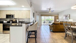 A modern kitchen with a central island, a dining area with a table and chairs, and a living room with a sofa and a TV.