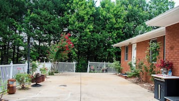 A residential backyard with a brick house, a white fence, potted plants, and a concrete patio.