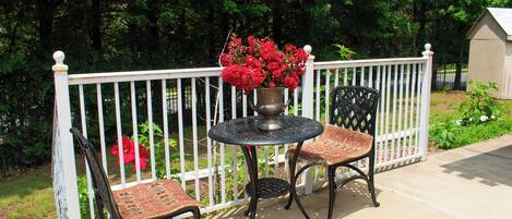 A patio with a round table and two chairs, a white fence, and a shed in the background.