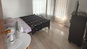 A bedroom with a bed, a desk, a chair, a fan, and a dresser.