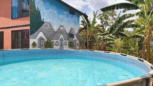 A swimming pool with a tiled edge, a mural on the adjacent building, and tropical vegetation.