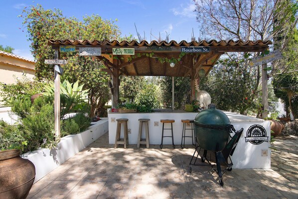 An outdoor bar area with a grill, stools, and a sign for 'Mondo's Pizza'.
