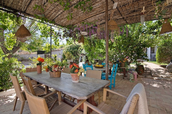 Une terrasse extérieure avec une table et des chaises, entourée de plantes en pot et de décorations suspendues.