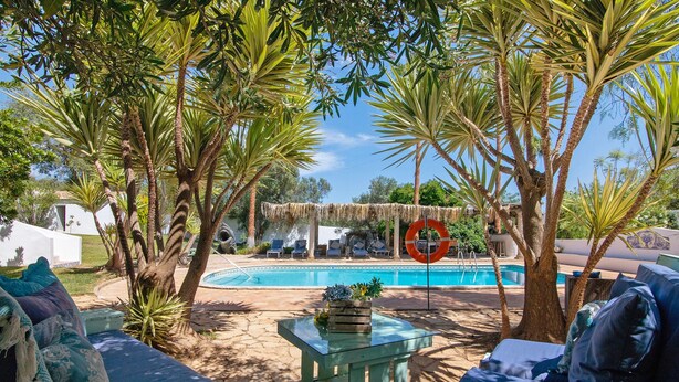 A poolside area with lounge chairs, a glass table, and a thatched umbrella. - Apartment 'Casa De Mondo - Blue Room' with Shared Pool, Wi-Fi and Air Conditioning (Boliqueime)