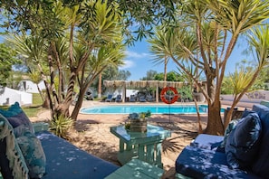 Un espace aménagé au bord de la piscine, avec des chaises longues, une table en verre et un parasol en chaume.