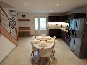 Een moderne keuken met een eethoek, met een ronde tafel met stoelen, een inbouwoven en een koelkast.