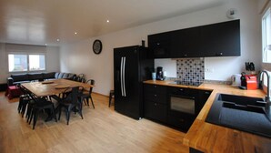 A modern kitchen with black cabinets, a wooden dining table, and a built-in oven. - La Ferme Aux Deux Chevaux 1 (Francheville)