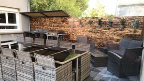 An outdoor patio with wicker furniture, a barbecue grill, and a wooden wall with potted plants. - La Ferme Aux Deux Chevaux 1 (Francheville)