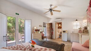 A bedroom with a bed, a ceiling fan, a bench, and a view through the door.