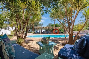 Un espace aménagé au bord de la piscine, avec des chaises longues, une table en verre et un parasol en chaume.
