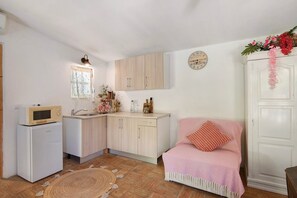 Une cuisine compacte équipée d’un four à micro-ondes, d’un évier et de meubles en bois. On peut apercevoir une petite fenêtre avec des rideaux à motifs et une horloge au mur.