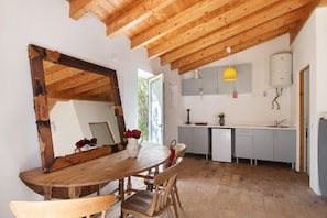 Une cuisine rustique avec une table à manger en bois, des chaises, un grand miroir, une suspension jaune et un chauffe-eau.