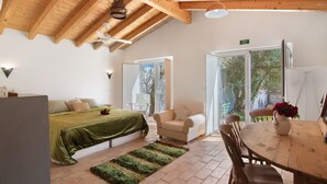 A room with a bed, a chair, a table, and a view of the outdoors.